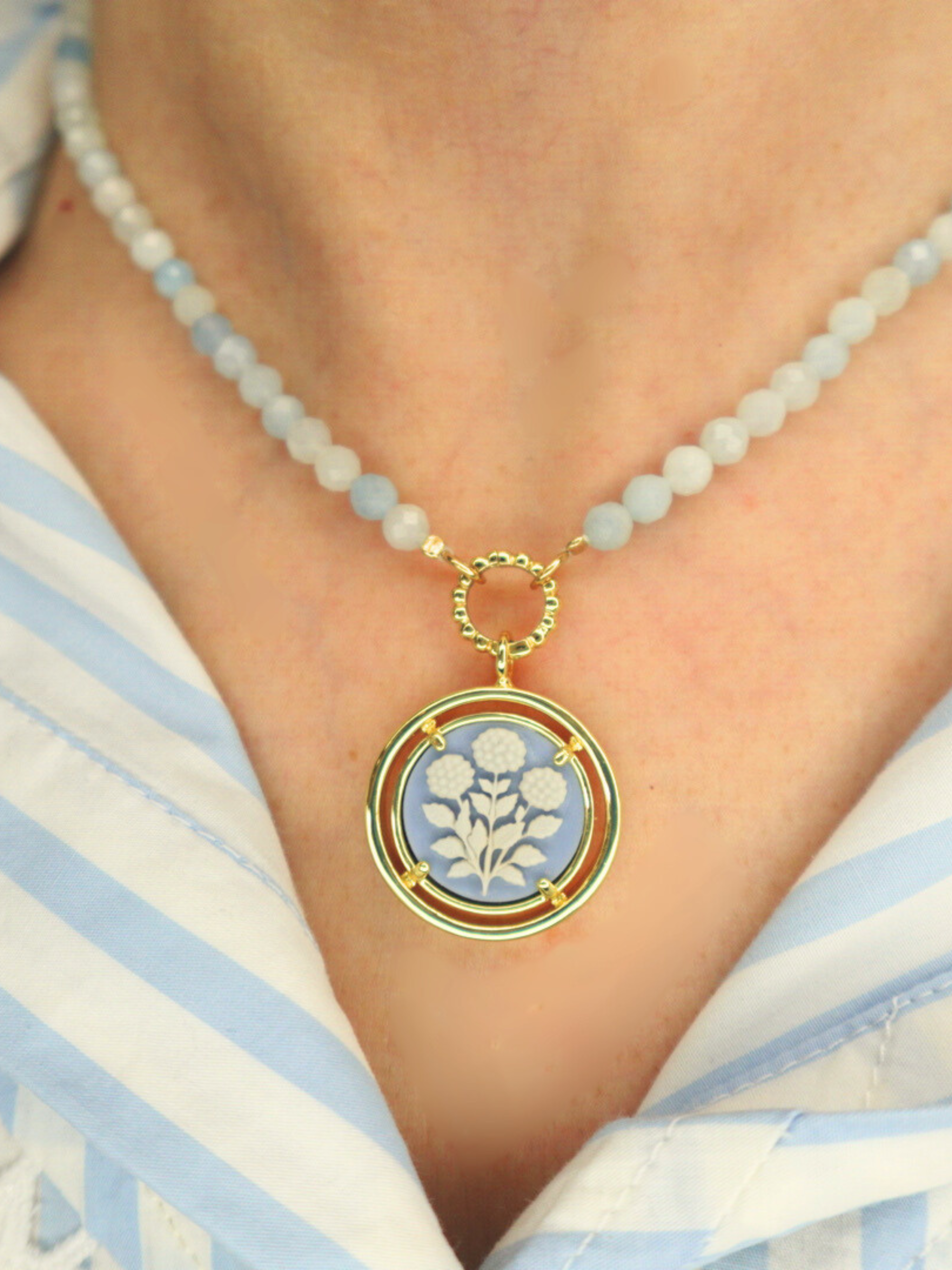 Necklace with a cameo floral pendant on a person wearing a striped shirt