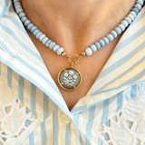 blue beaded necklace with a floral cameo pendant worn by a person in a striped shirt