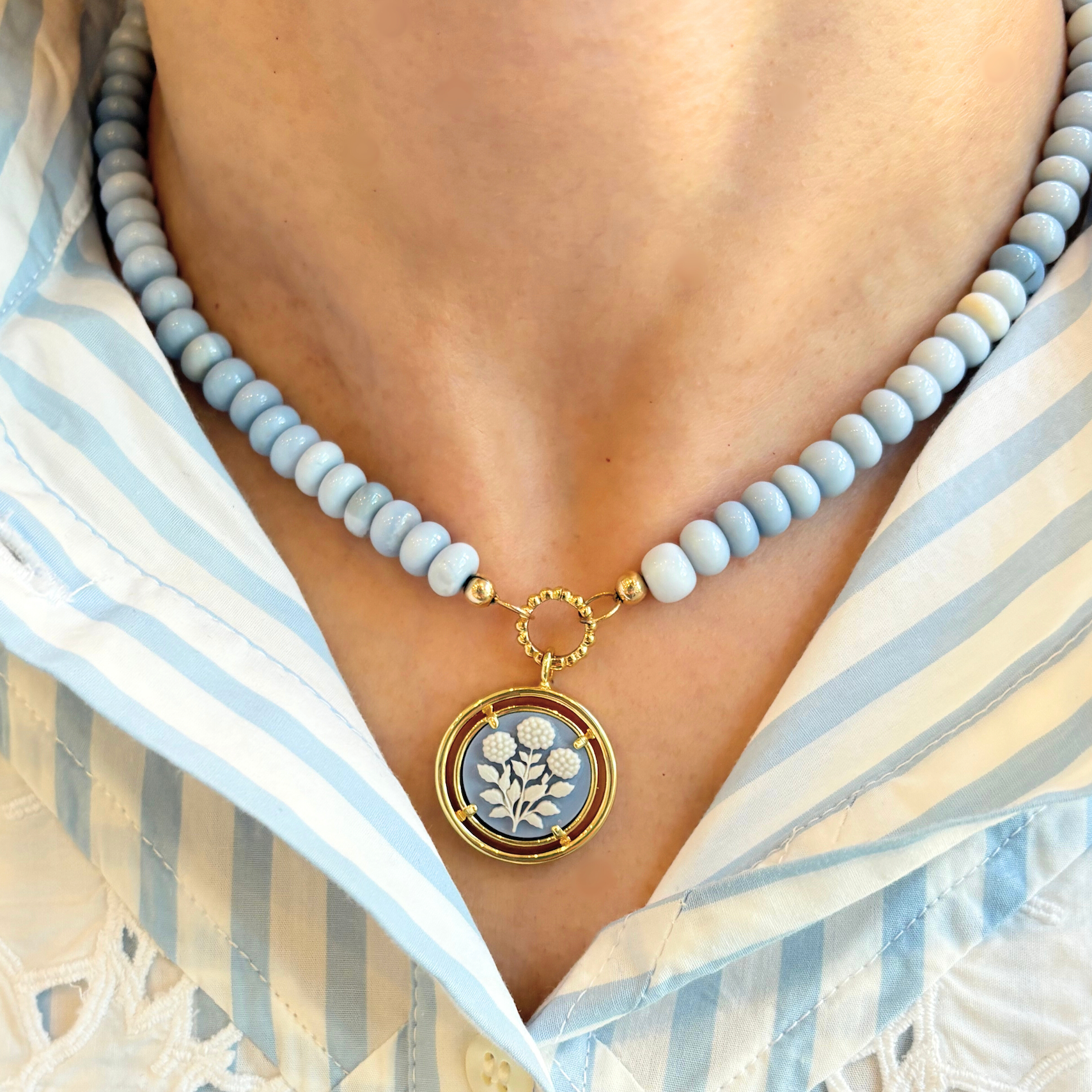 blue beaded necklace with a floral cameo pendant worn by a person in a striped shirt