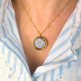 Blue cameo pendant necklace worn by a person in a blue and white striped shirt.