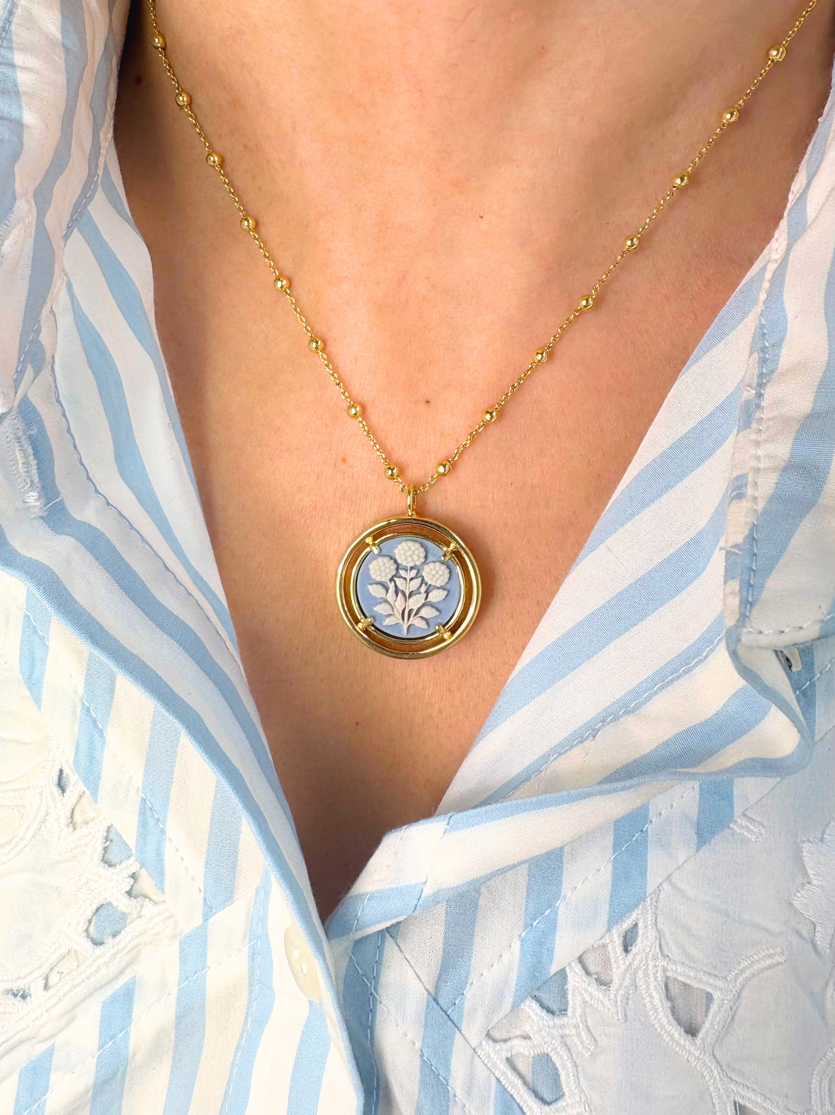 Blue cameo pendant necklace worn by a person in a blue and white striped shirt.