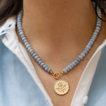 Close-up of a person wearing a blue beaded necklace with a gold pendant.