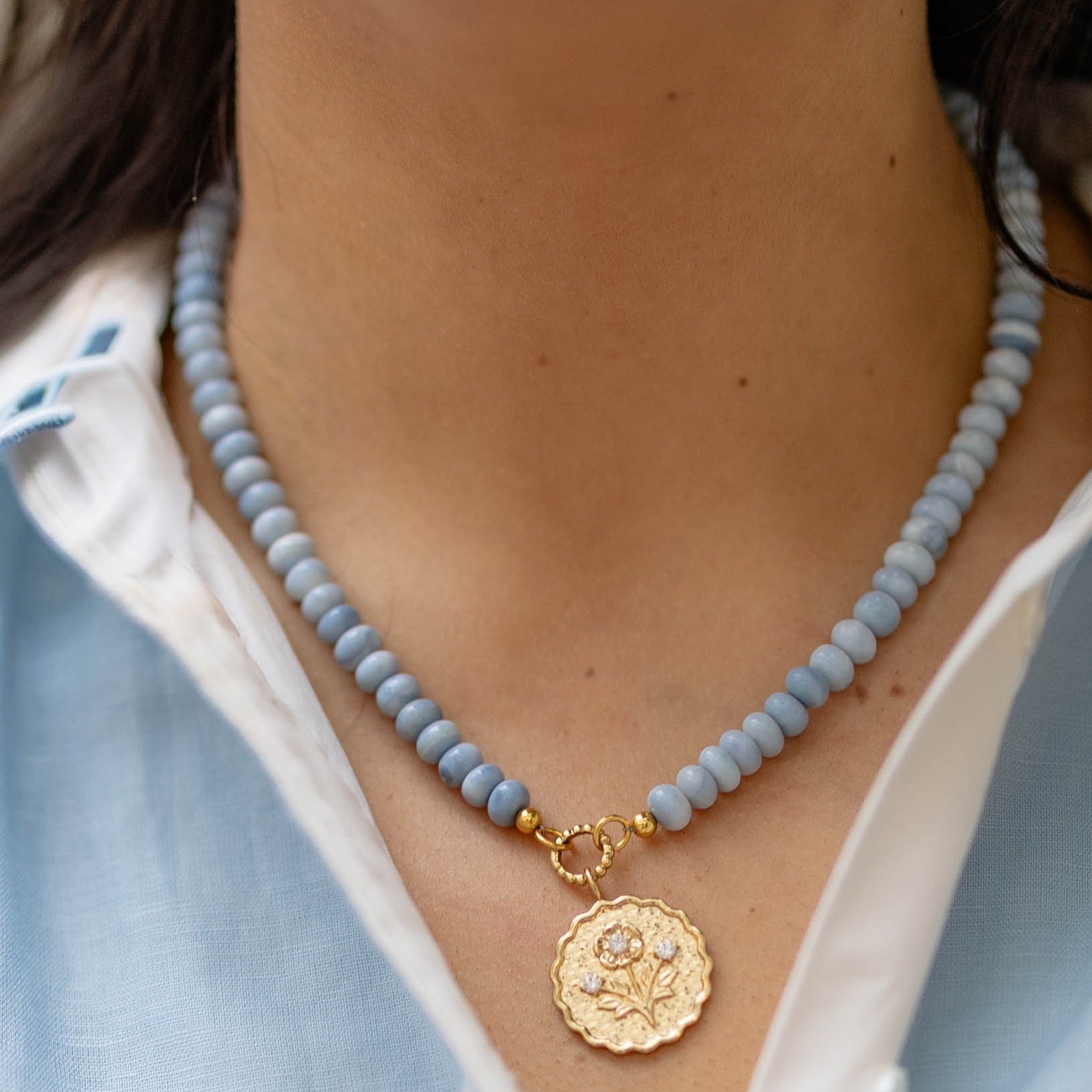 Close-up of a person wearing a blue beaded necklace with a gold pendant.