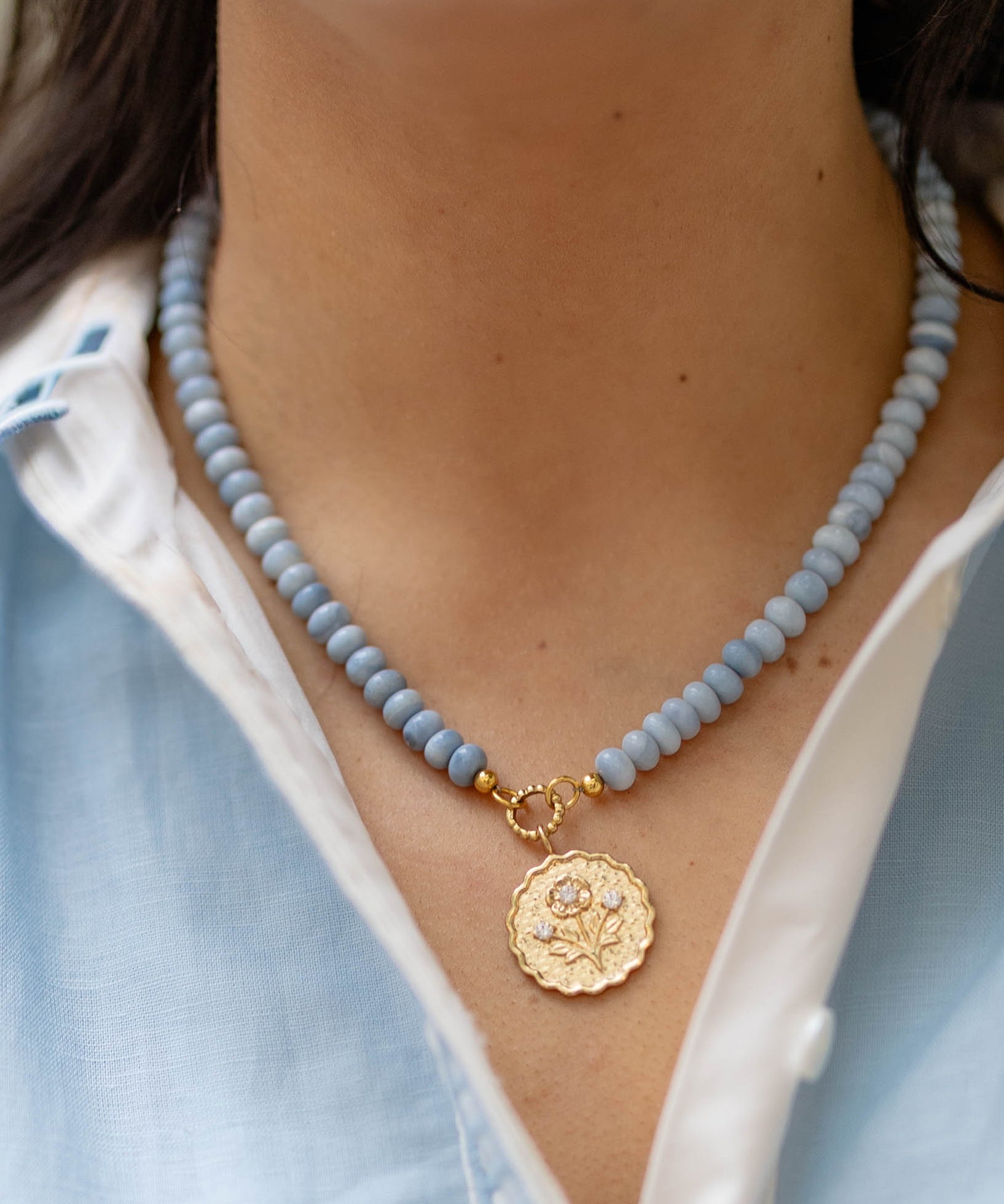Close-up of a person wearing a blue beaded necklace with a gold pendant.
