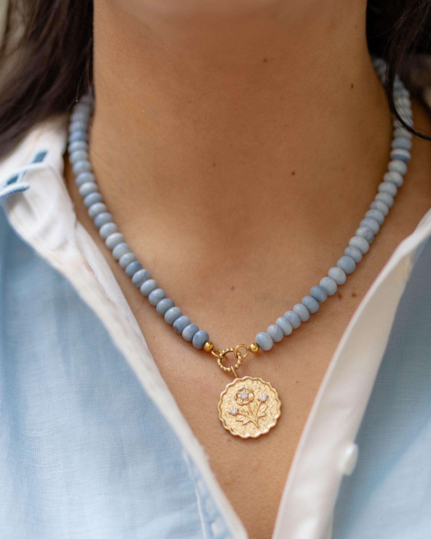 Close-up of a person wearing a blue beaded necklace with a gold pendant.