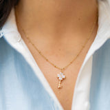 clover key charm on a gold chain on a person wearing a blue and white shirt