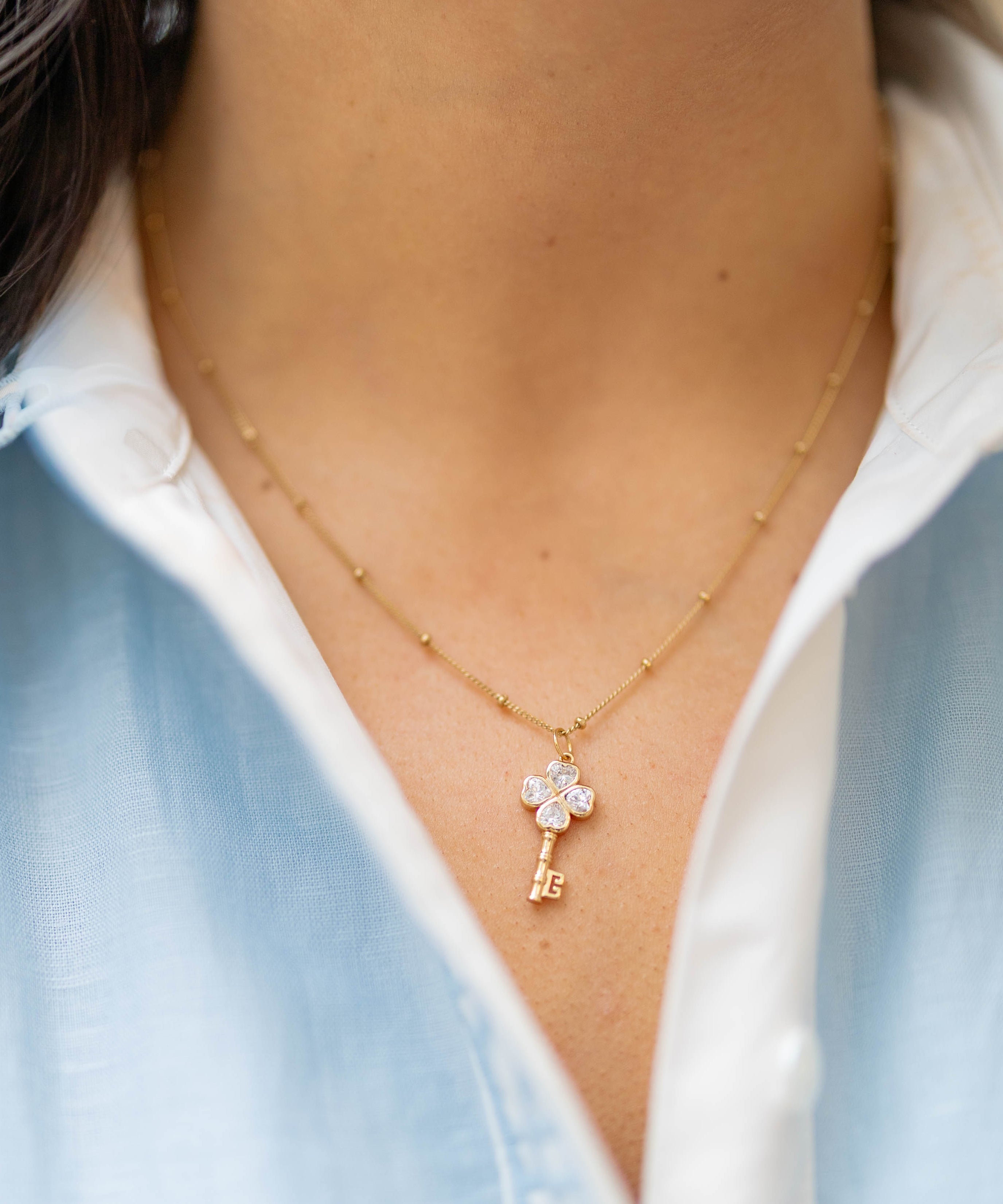 clover key charm on a gold chain on a person wearing a blue and white shirt