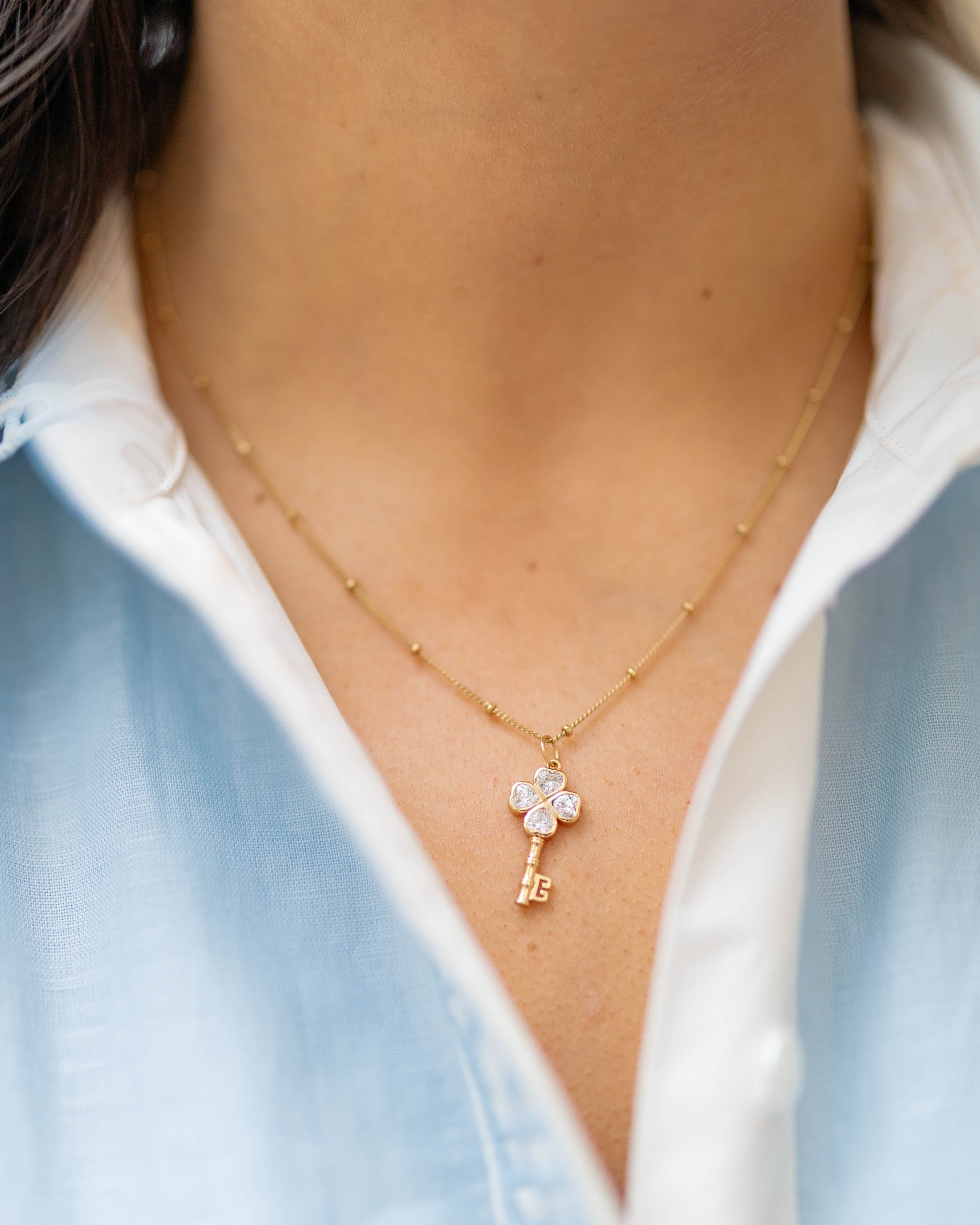 clover key charm on a gold chain on a person wearing a blue and white shirt