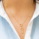 a gold key charm on a gold chain on a woman in a blue and white shirt