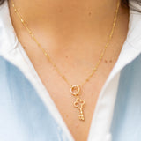 a gold key charm on a gold chain on a woman in a blue and white shirt