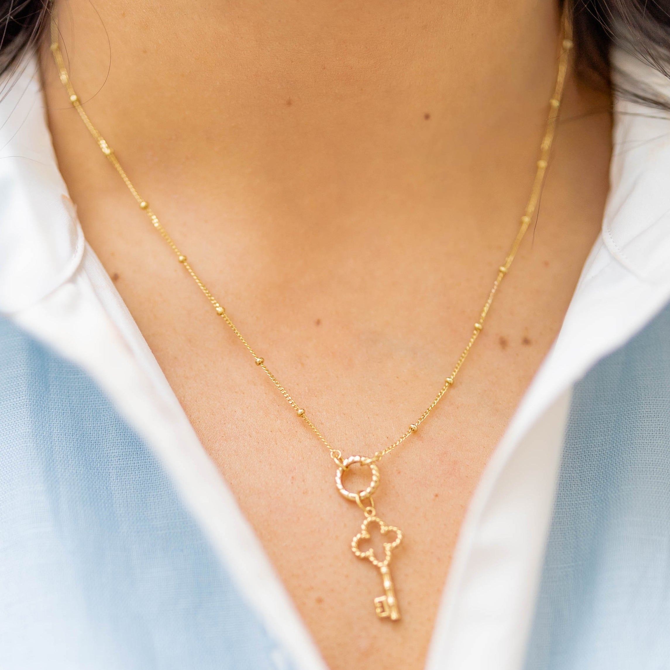a gold key charm on a gold chain on a woman in a blue and white shirt