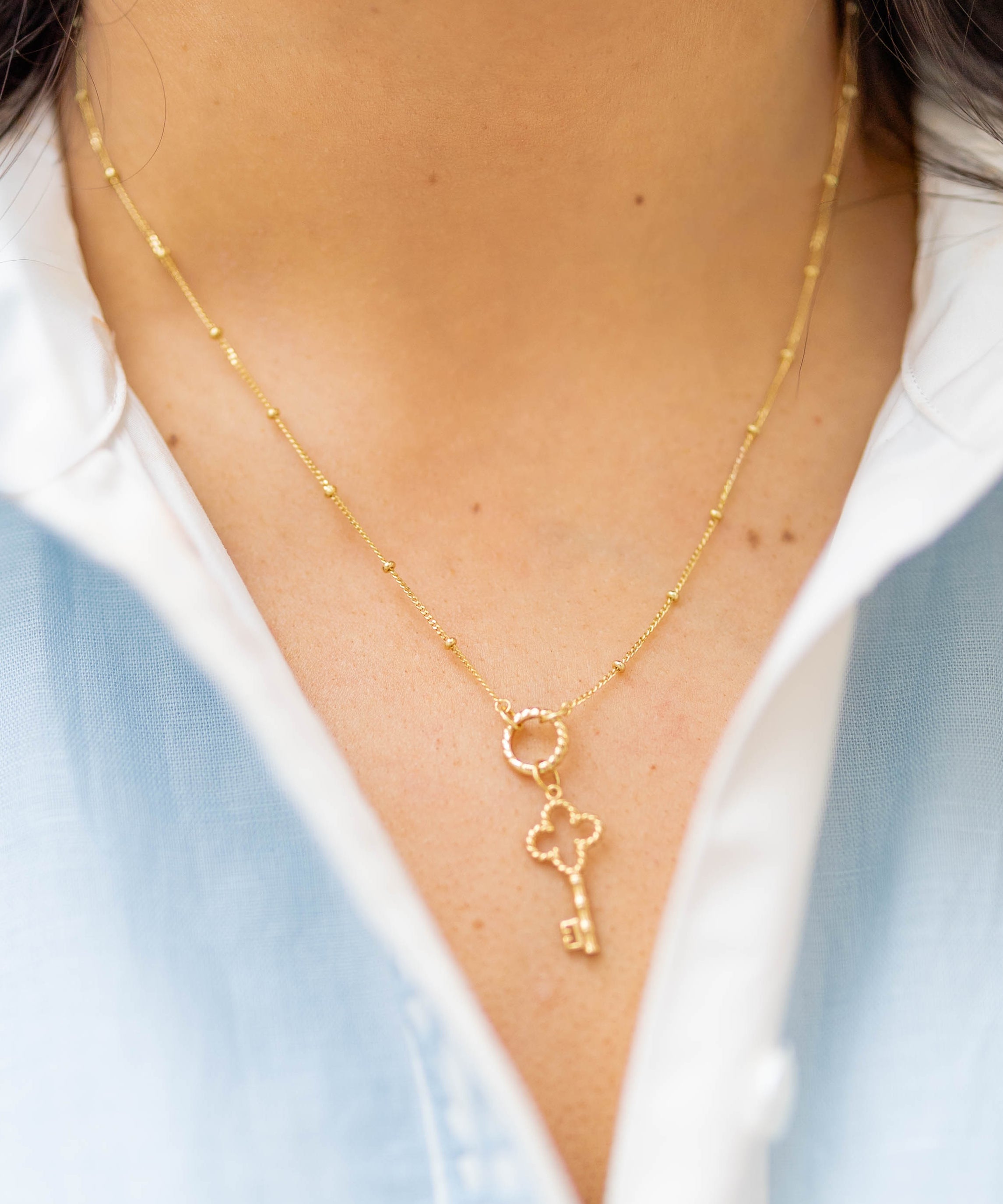 a gold key charm on a gold chain on a woman in a blue and white shirt