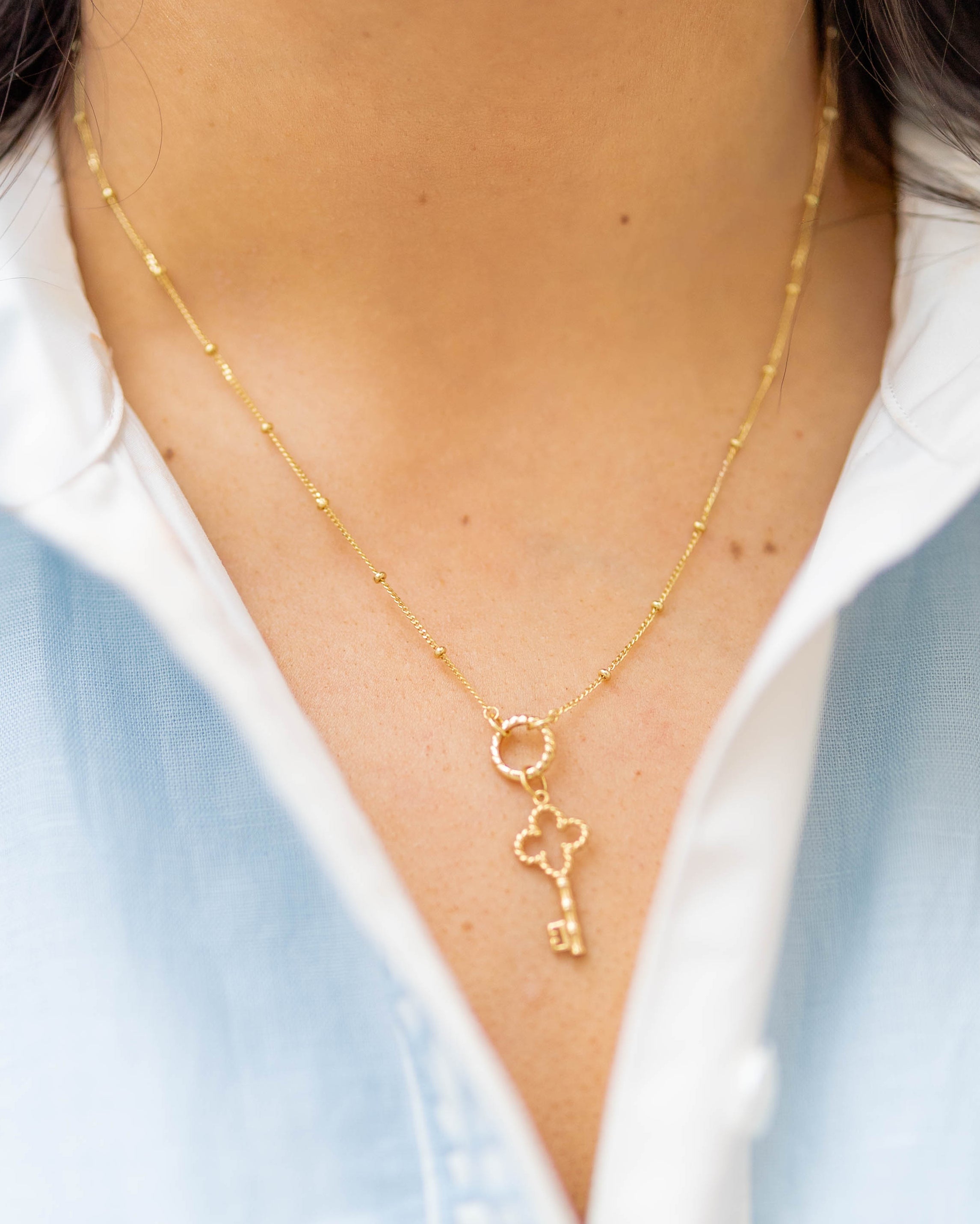 a gold key charm on a gold chain on a woman in a blue and white shirt