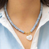 moonstone heart charm on a blue beaded necklace on a woman wearing a blue and white shirt