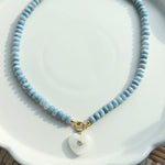 necklace with blue beads and heart shaped pendant on white tray
