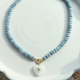 necklace with blue beads and heart shaped pendant on white tray