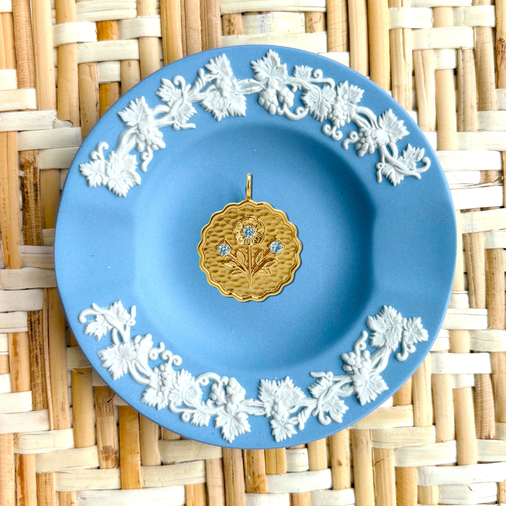 Blue decorative plate with white floral patterns and a gold center on a woven mat background
