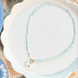 a moonstone shaped heart on a blue beaded necklace on a white plate