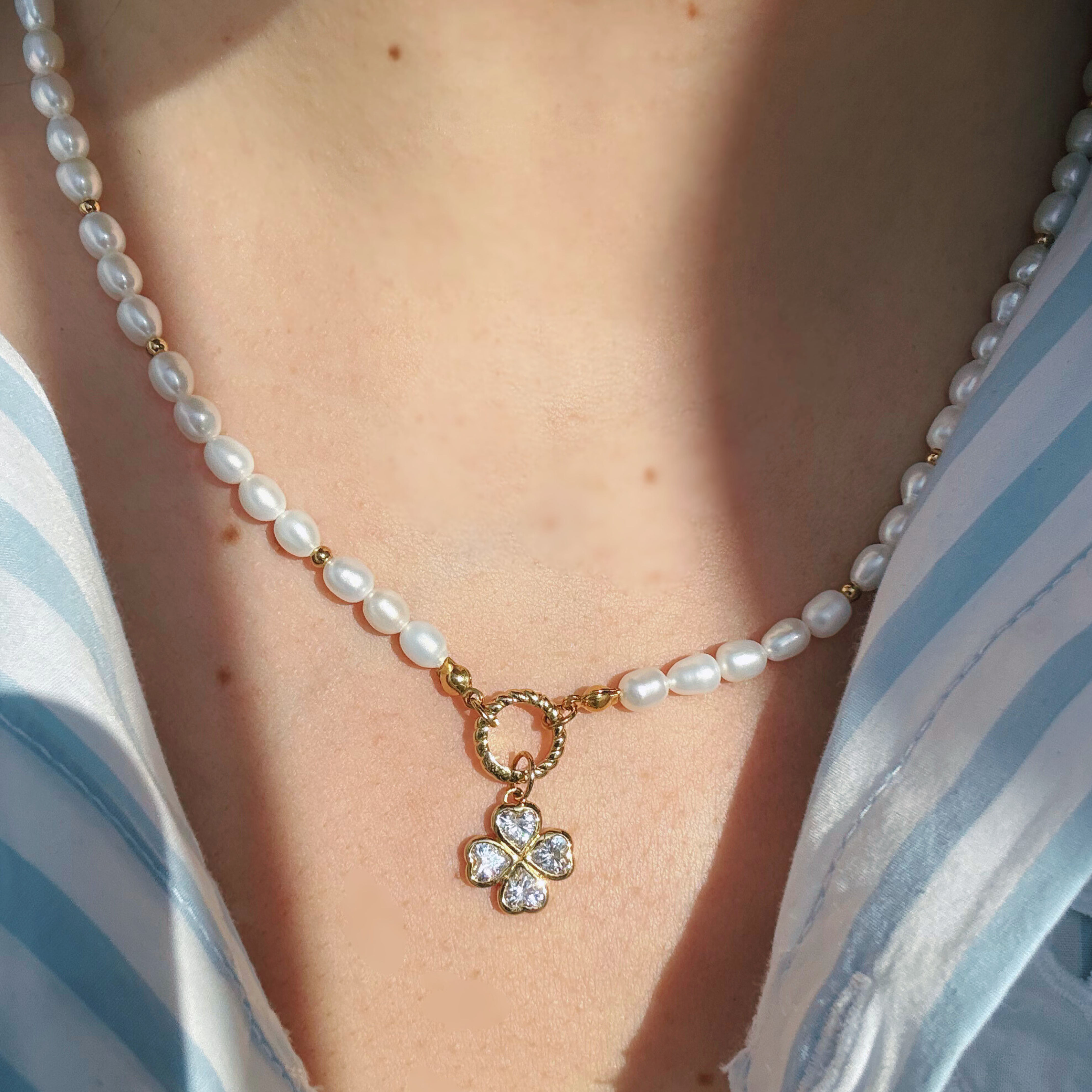 Pearl necklace with a clover-shaped charm worn by a person in a striped shirt.