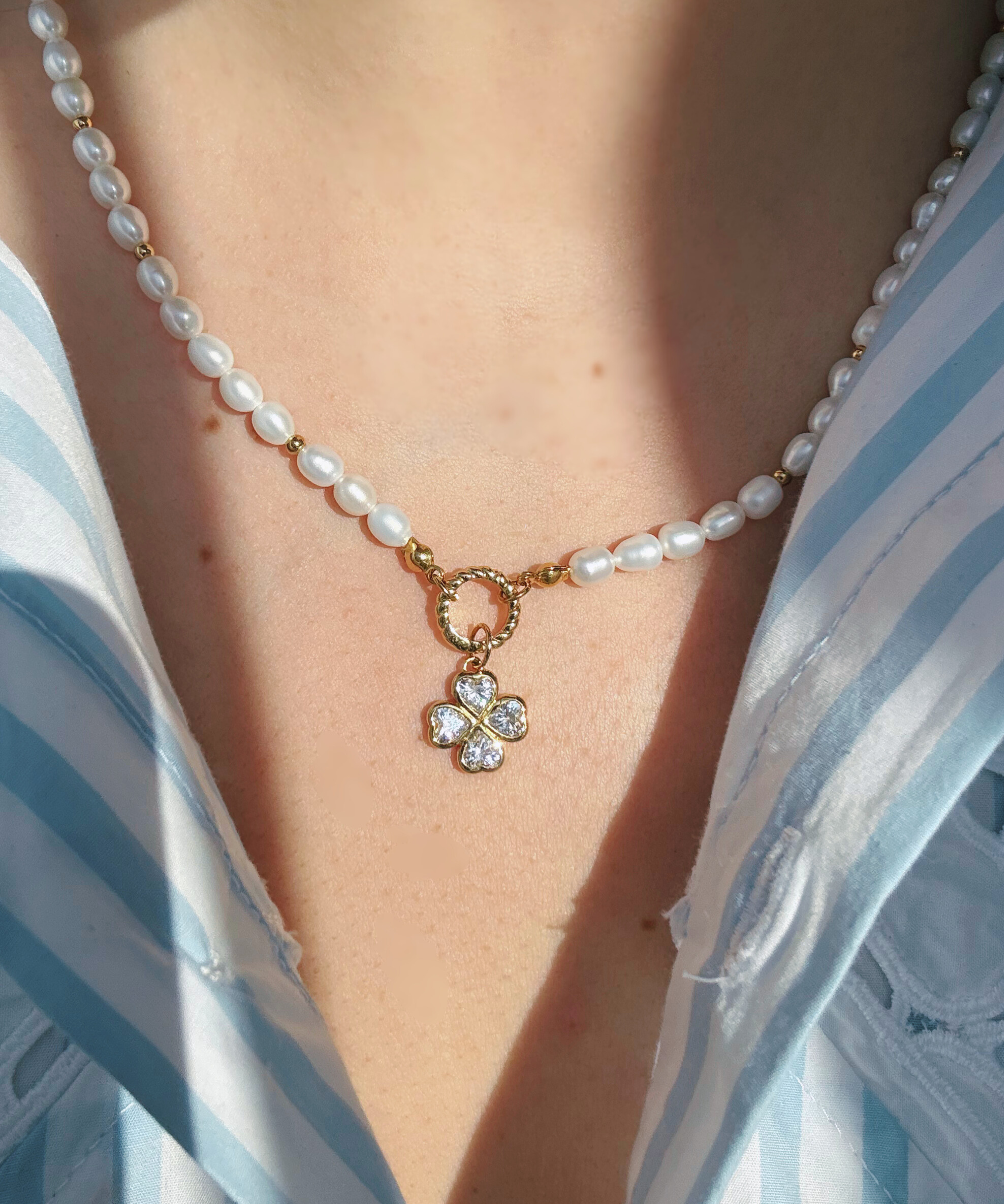 Pearl necklace with a clover-shaped charm worn by a person in a striped shirt.