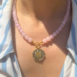 Necklace with pink beads and a decorative pendant on a person wearing a striped shirt.
