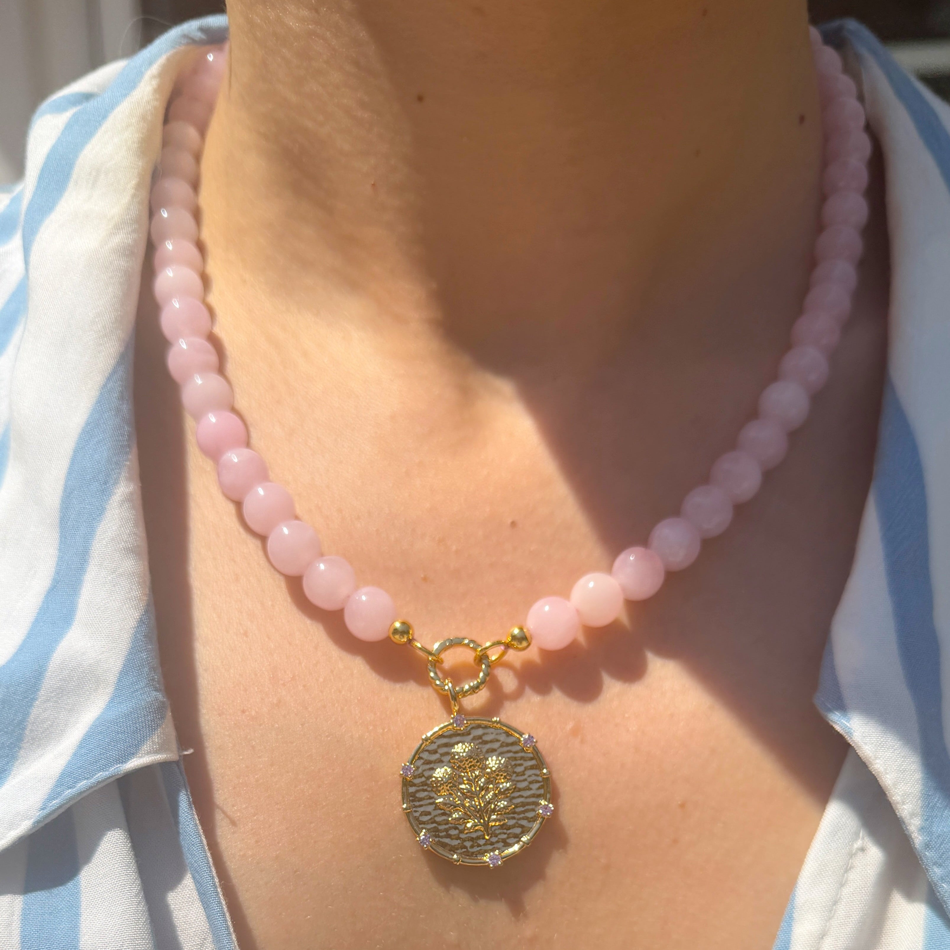 Necklace with pink beads and a decorative pendant on a person wearing a striped shirt.