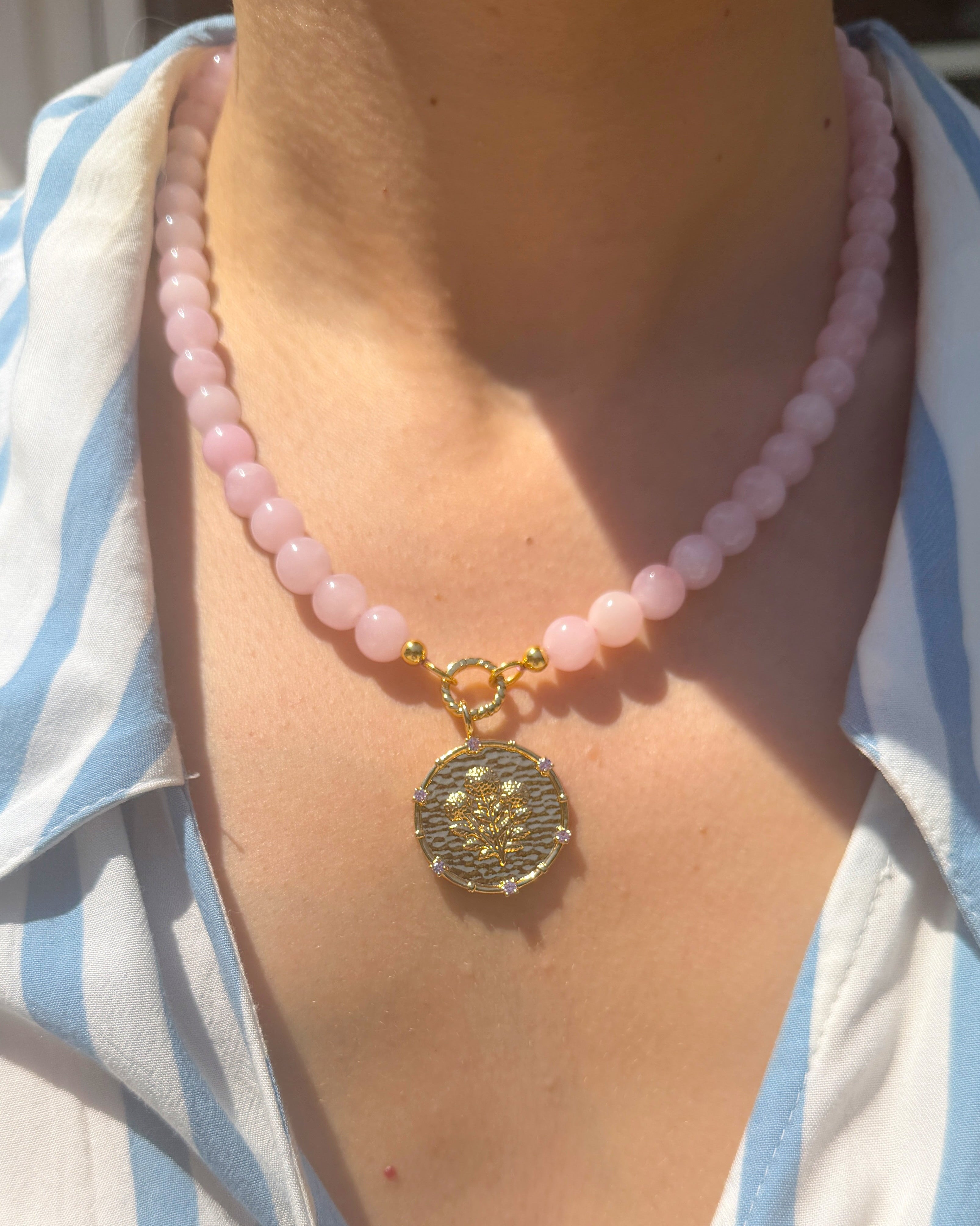 Necklace with pink beads and a decorative pendant on a person wearing a striped shirt.