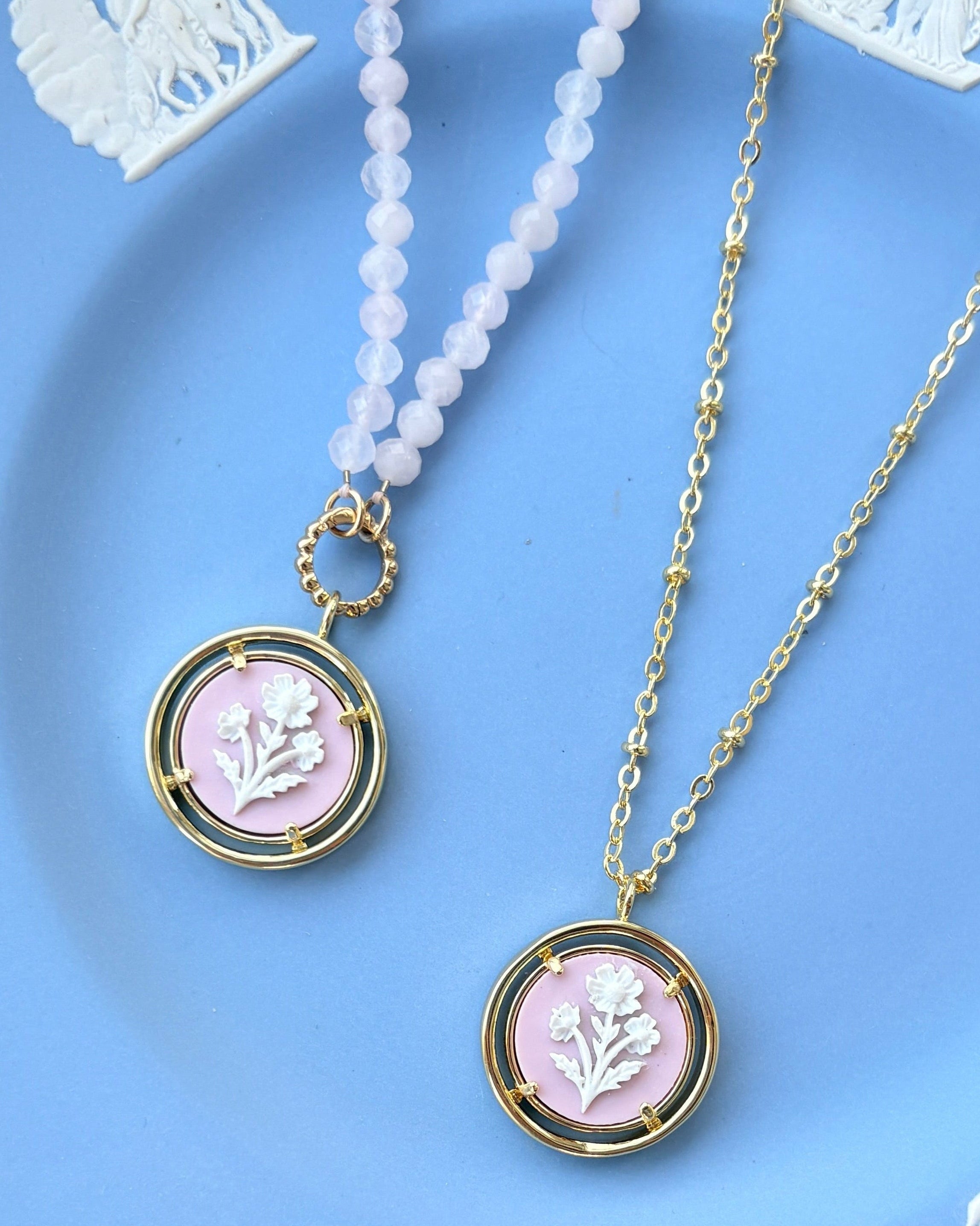 Two necklaces with pink pendants on a  blue plate.