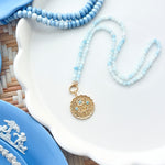 gold scalloped pendant charm on a blue gemstone strand of beads photographed on white tray