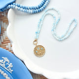 gold scalloped pendant charm on a blue gemstone strand of beads photographed on white tray