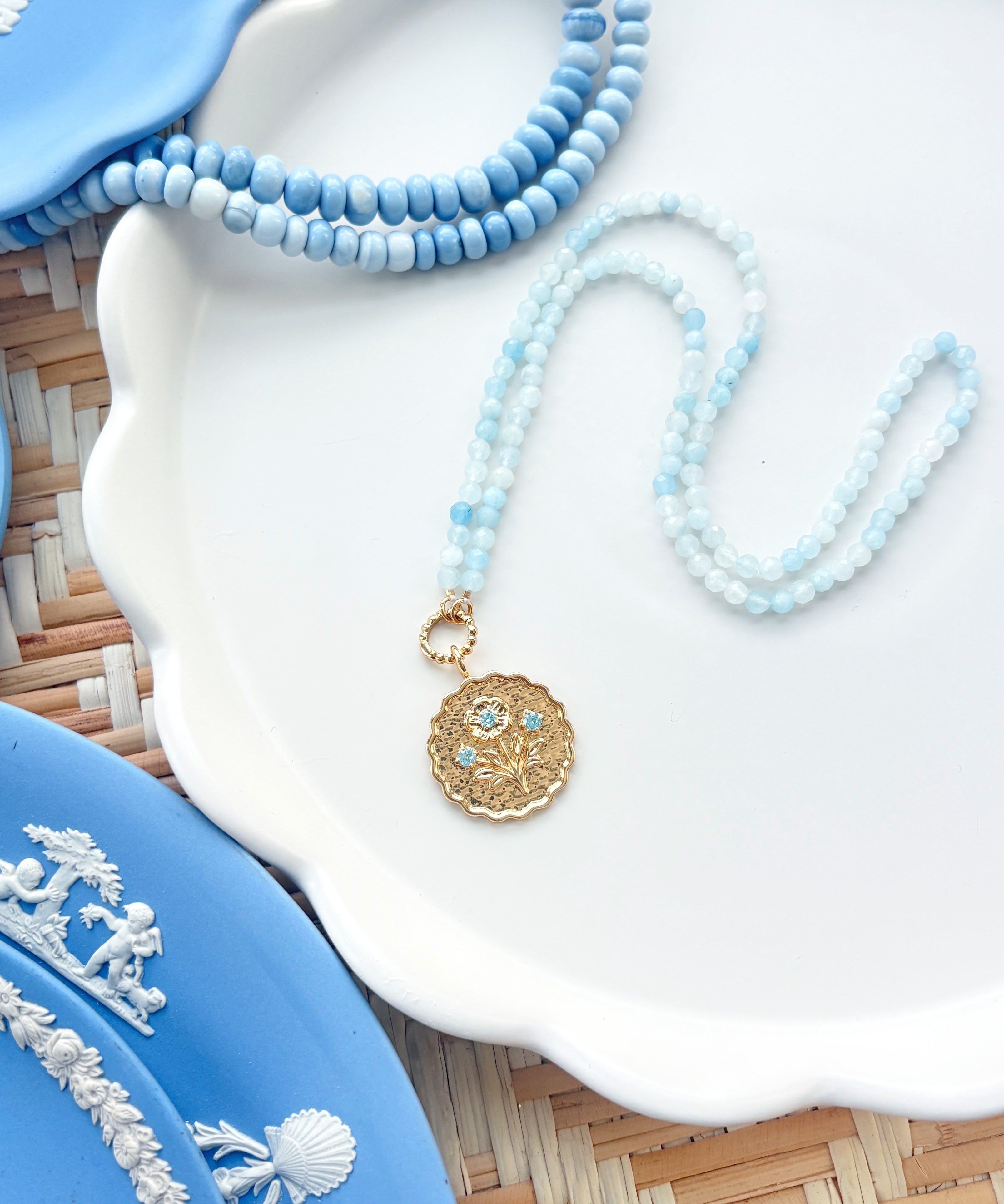 gold scalloped pendant charm on a blue gemstone strand of beads photographed on white tray