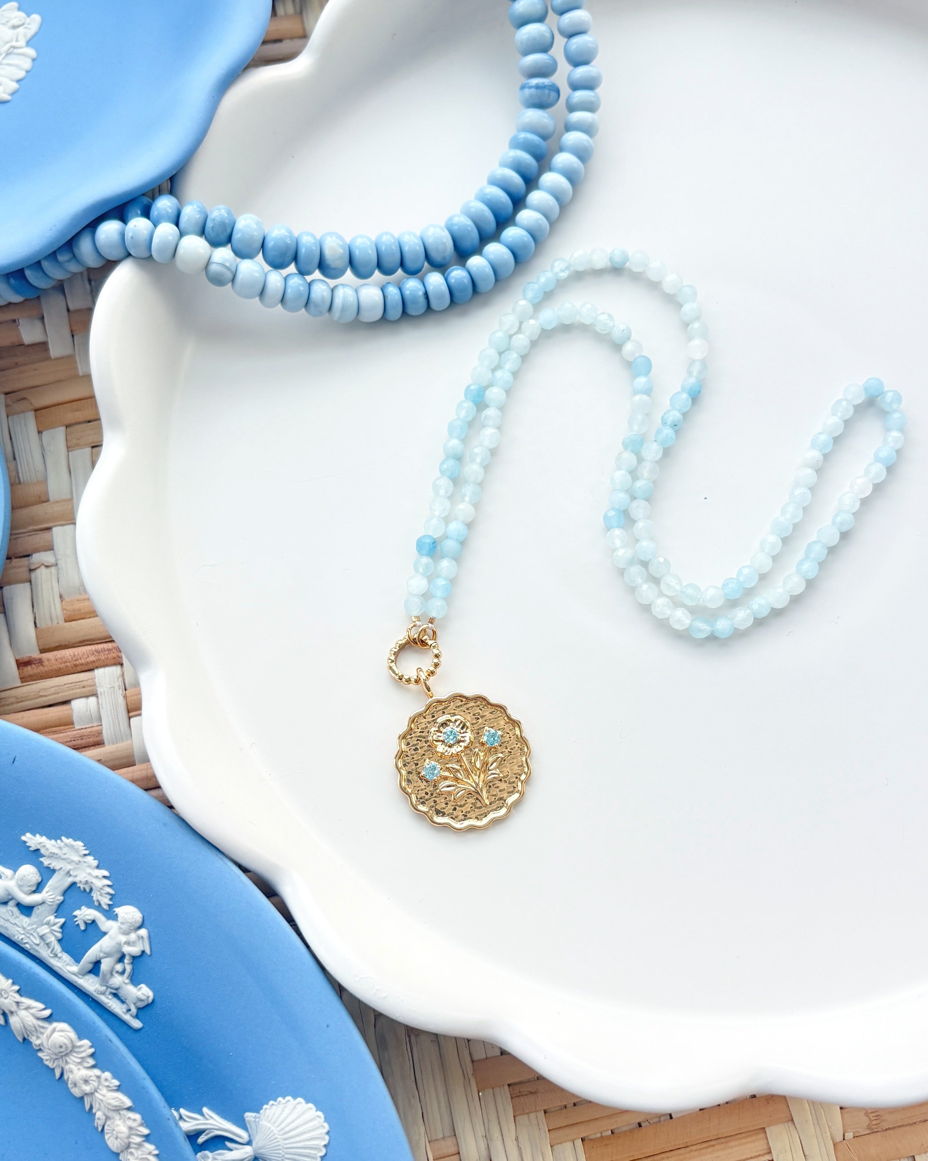 gold scalloped pendant charm on a blue gemstone strand of beads photographed on white tray