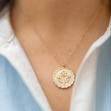 scalloped gold round pendant with a floral blossom on it with three gemstones on a gold chain on a woman