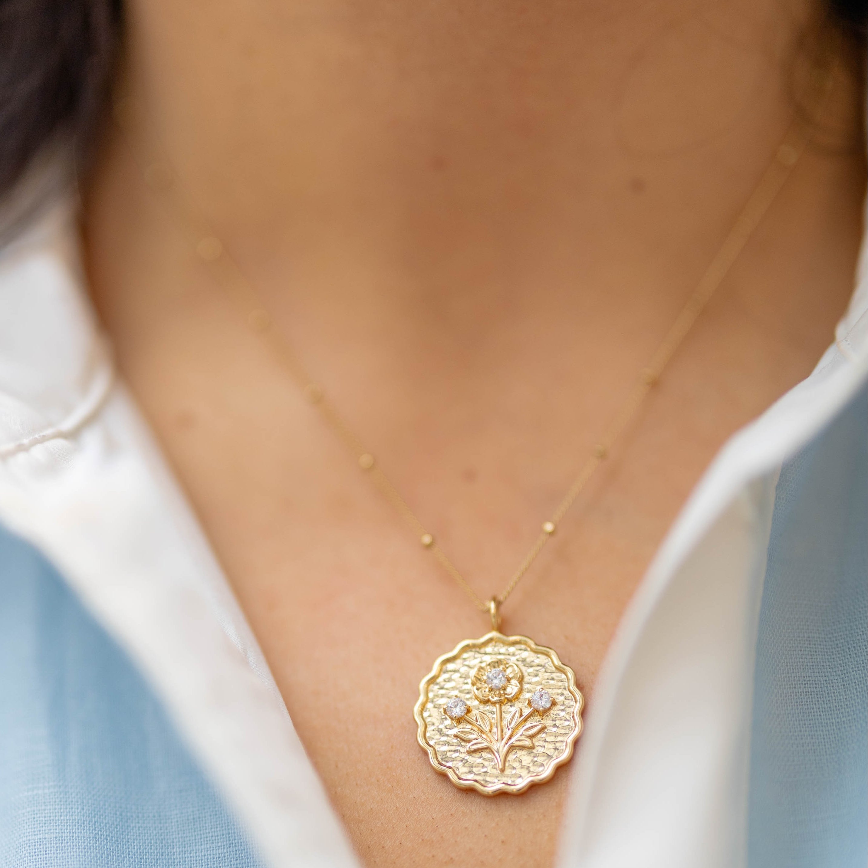 scalloped gold round pendant with a floral blossom on it with three gemstones on a gold chain on a woman