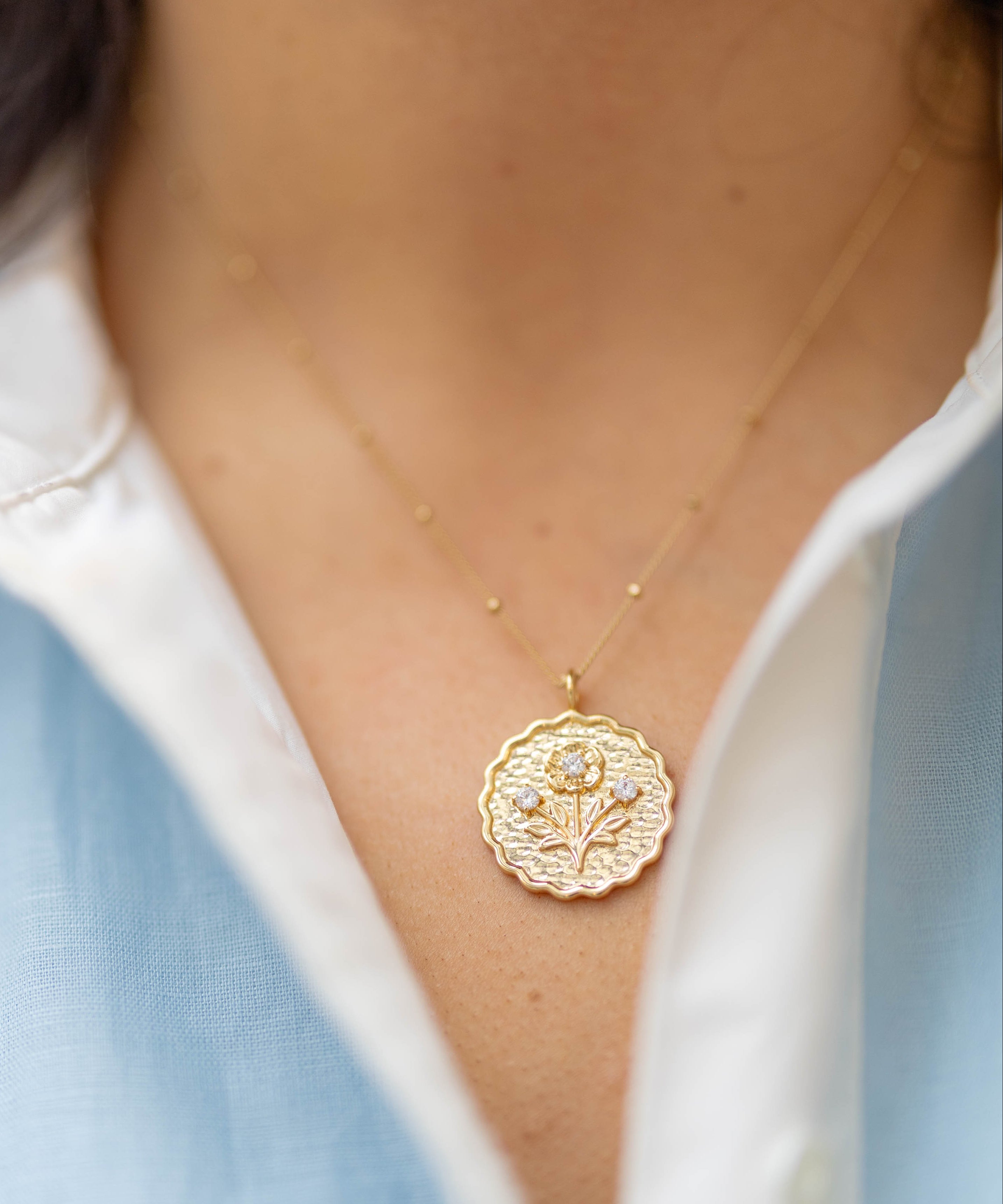 scalloped gold round pendant with a floral blossom on it with three gemstones on a gold chain on a woman