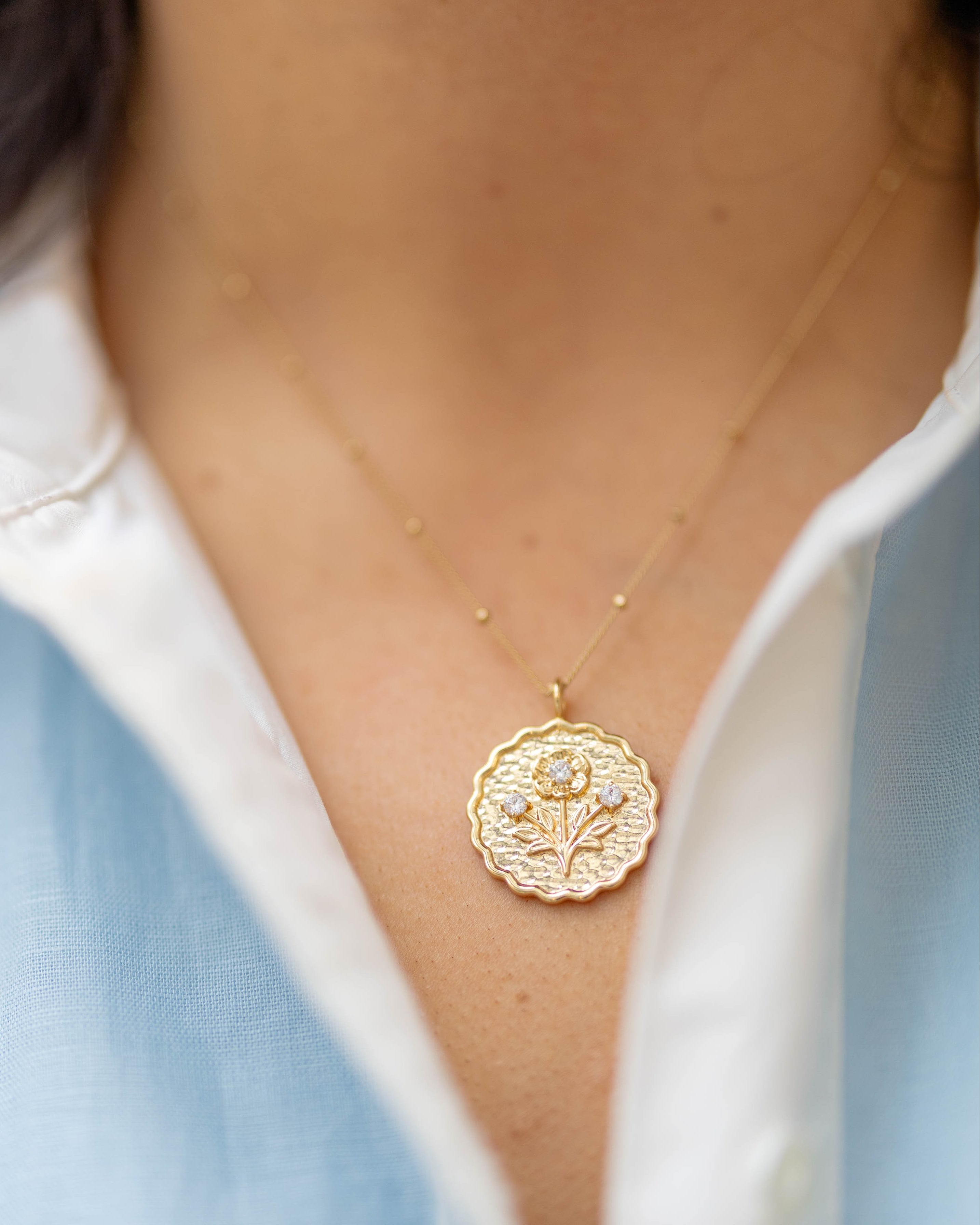 scalloped gold round pendant with a floral blossom on it with three gemstones on a gold chain on a woman