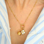golden necklace with a basket charm and clover charm on a person wearing a blue and white striped shirt