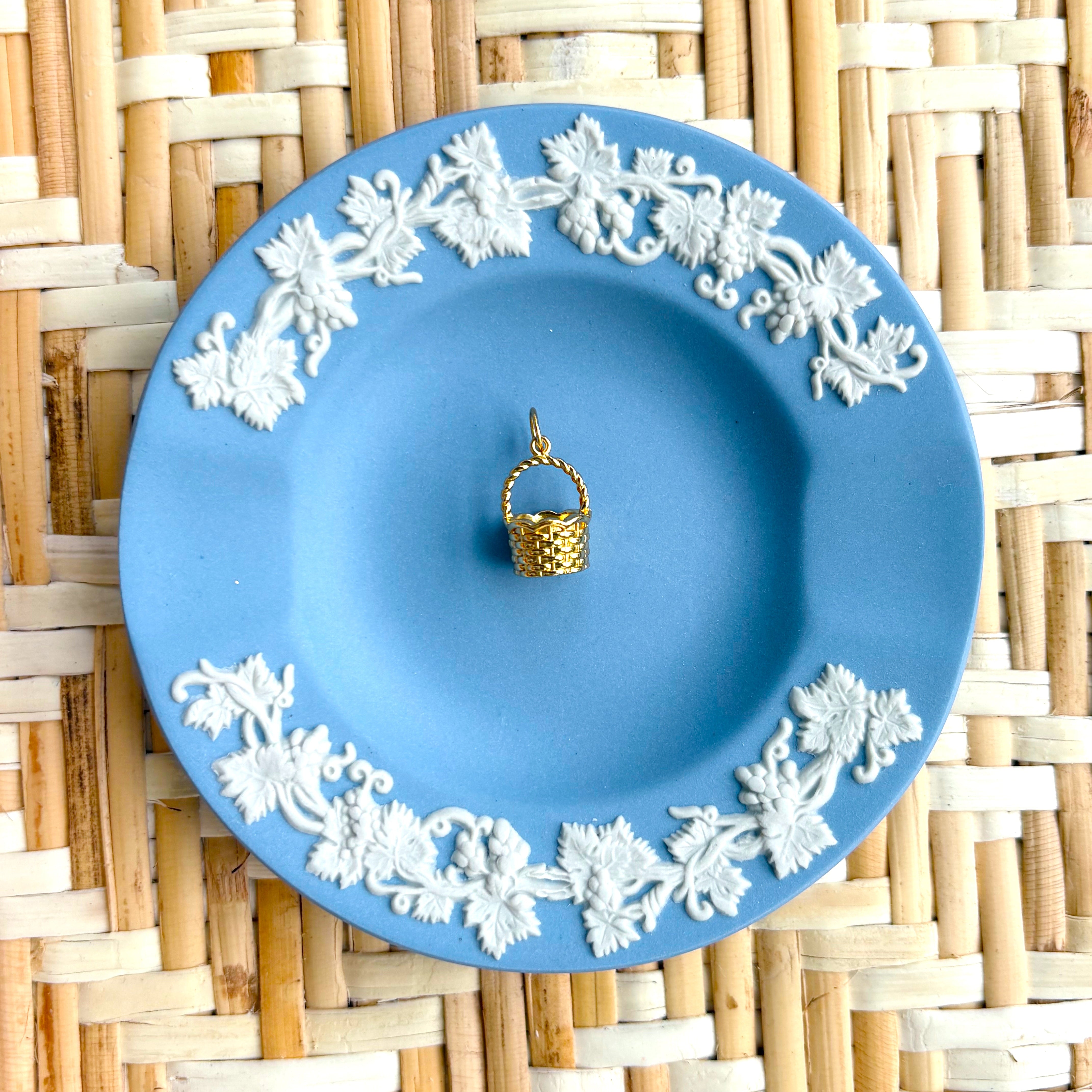 Blue decorative plate with white floral patterns on a woven mat displaying a golden basket charm