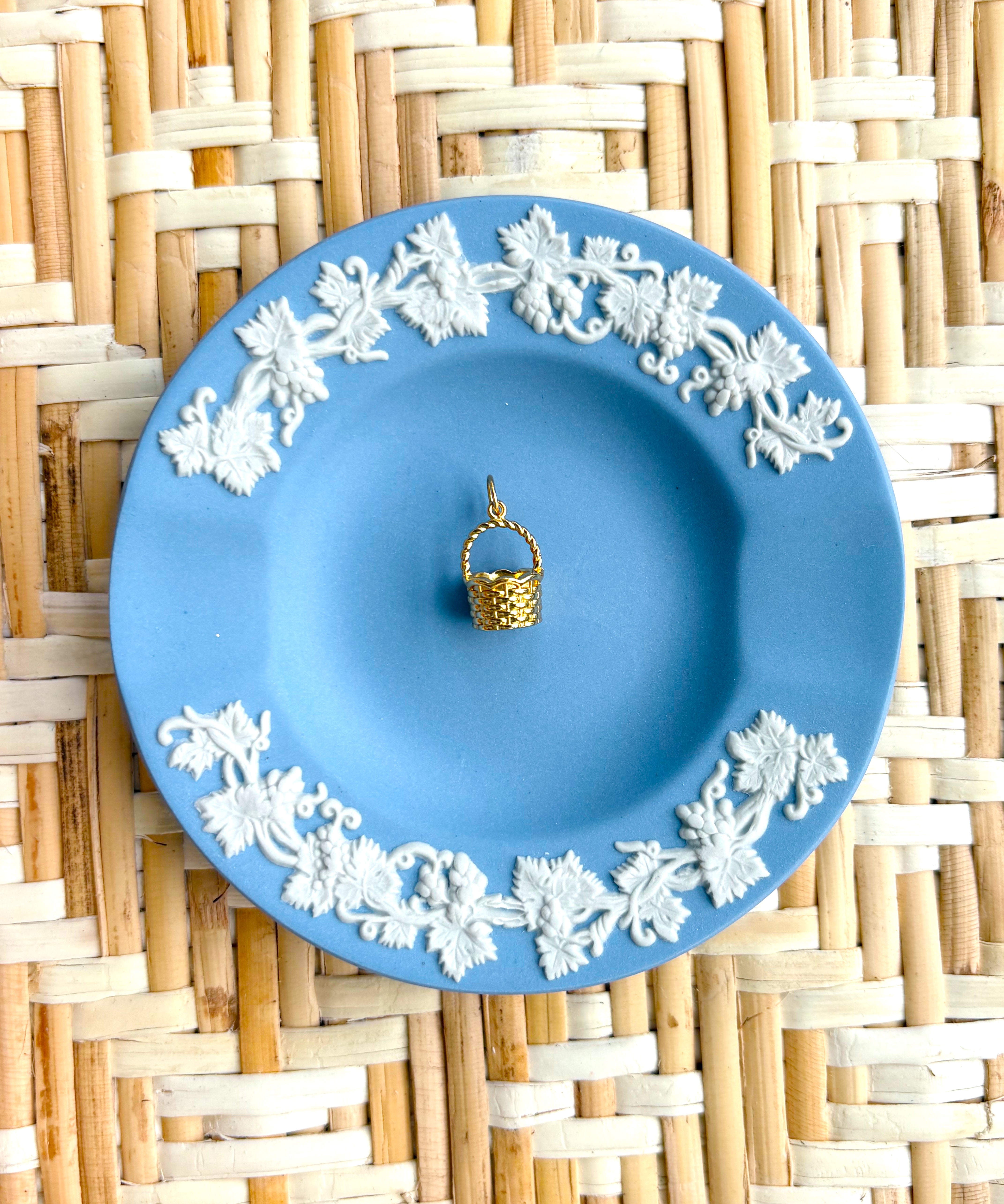 Blue decorative plate with white floral patterns on a woven mat displaying a golden basket charm