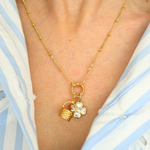 Golden necklace with a basket charm worn by a person in a blue and white striped shirt