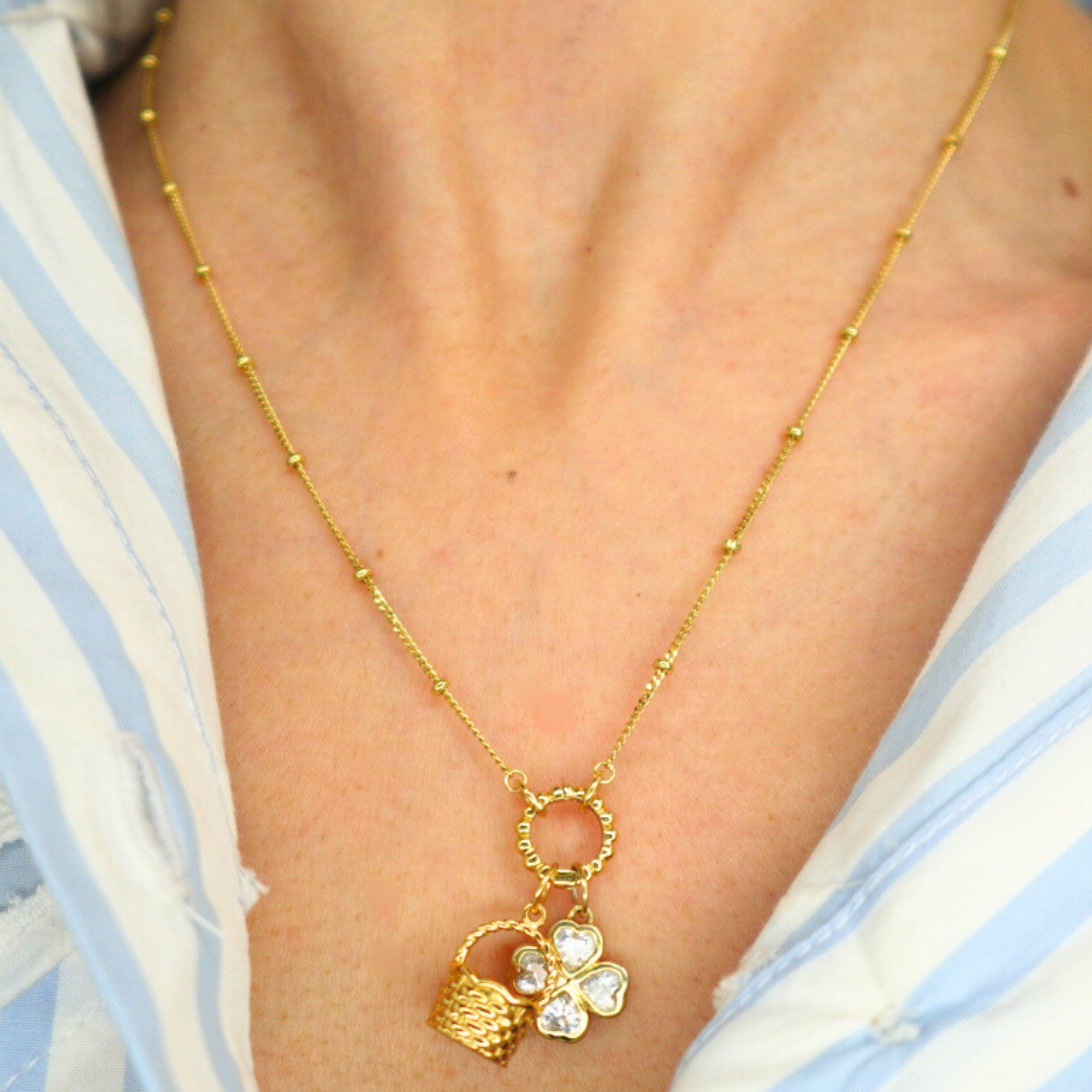 Golden necklace with a basket charm worn by a person in a blue and white striped shirt