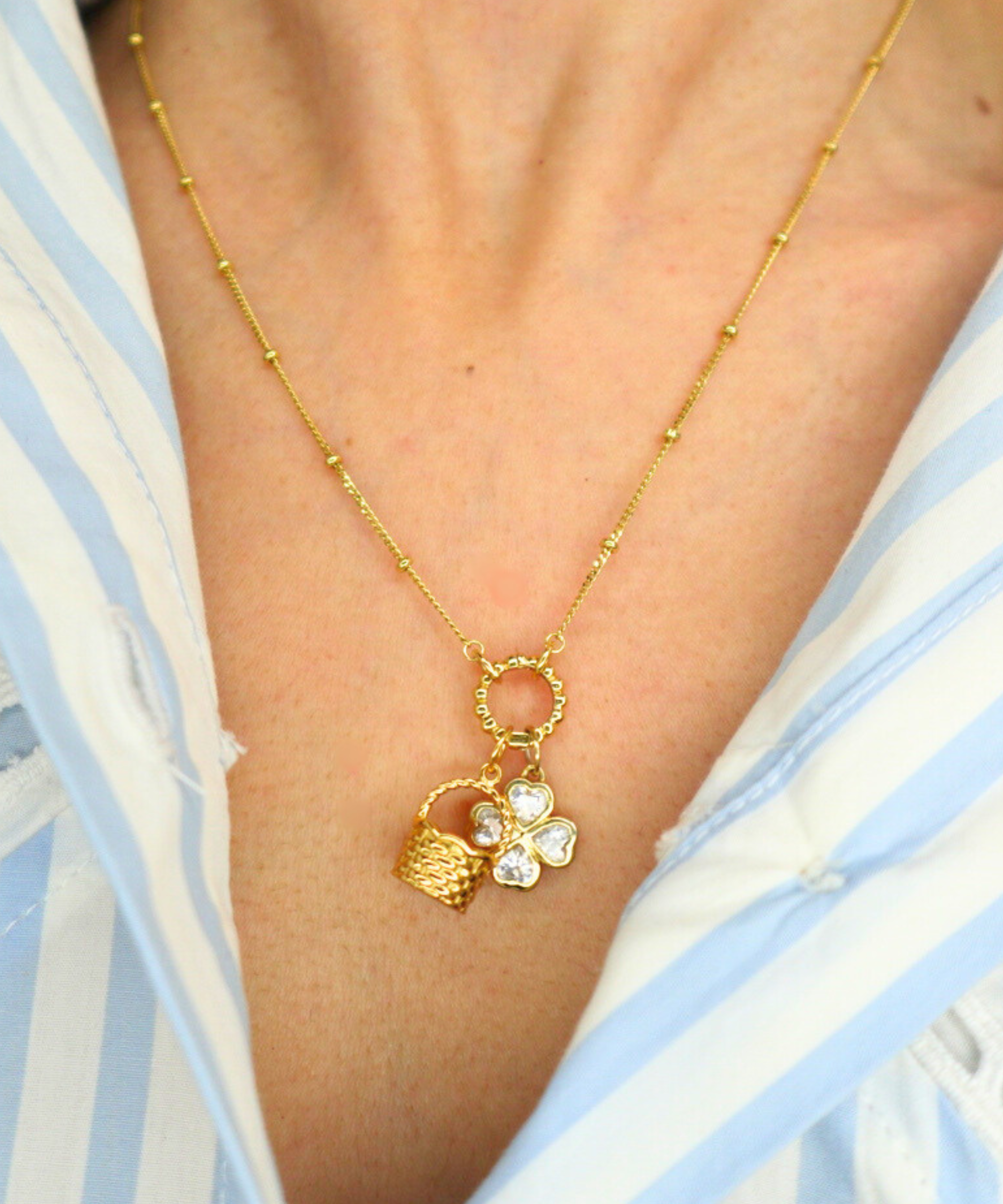 Golden necklace with a basket charm worn by a person in a blue and white striped shirt