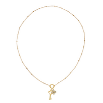 Golden necklace with a key-shaped charm and clover charm on a white background
