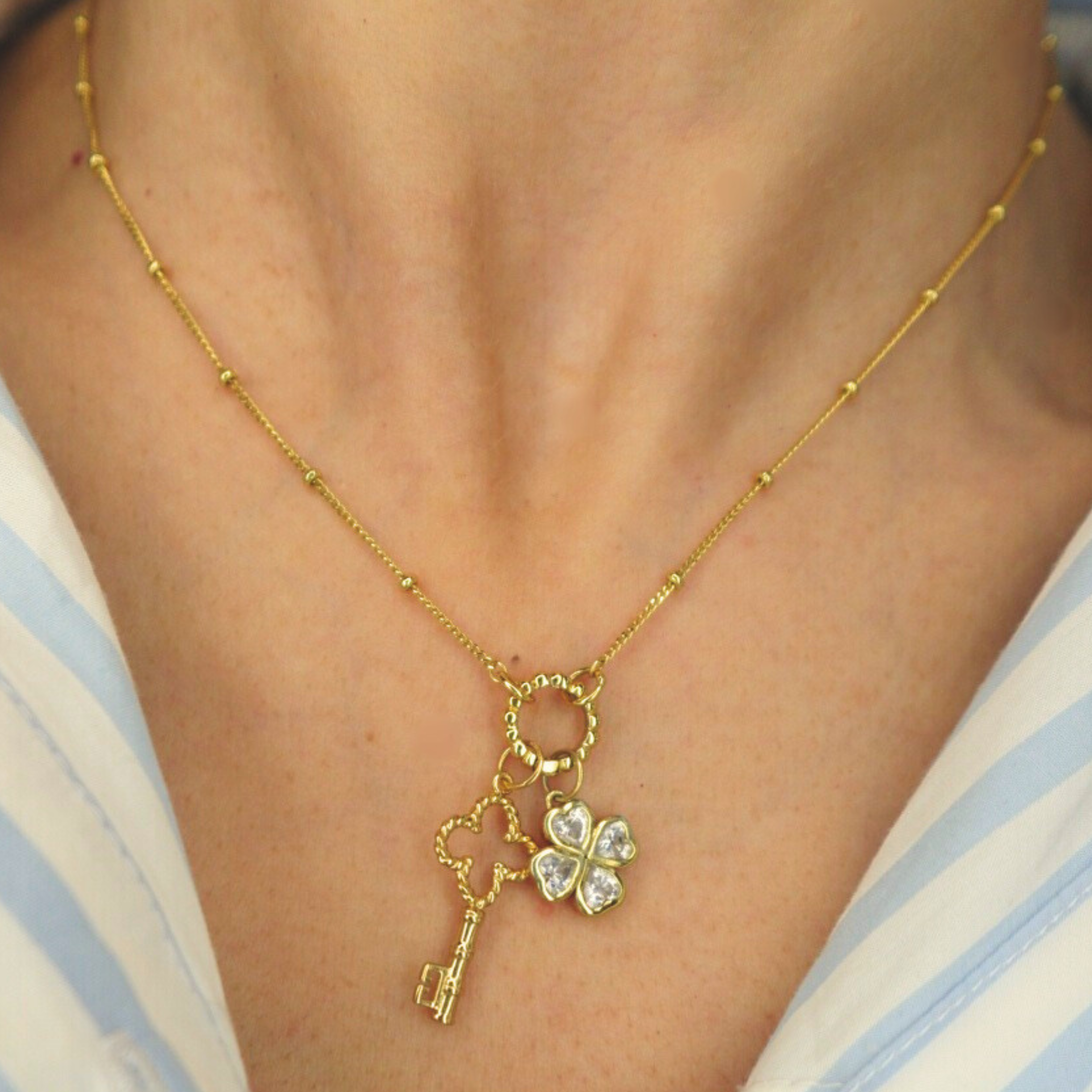 Golden necklace with a key and clover pendant on a person wearing a striped shirt
