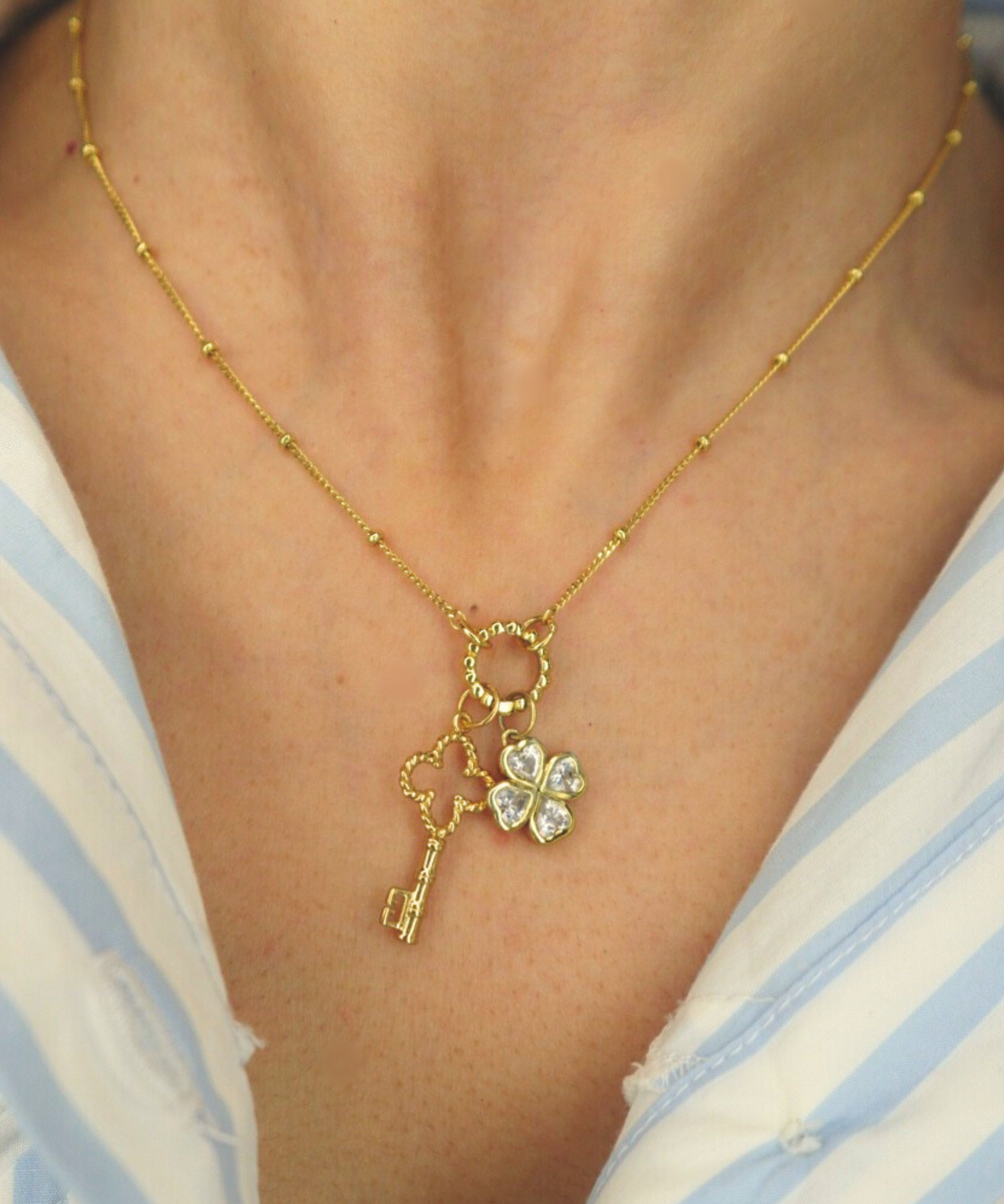 Golden necklace with a key and clover pendant on a person wearing a striped shirt