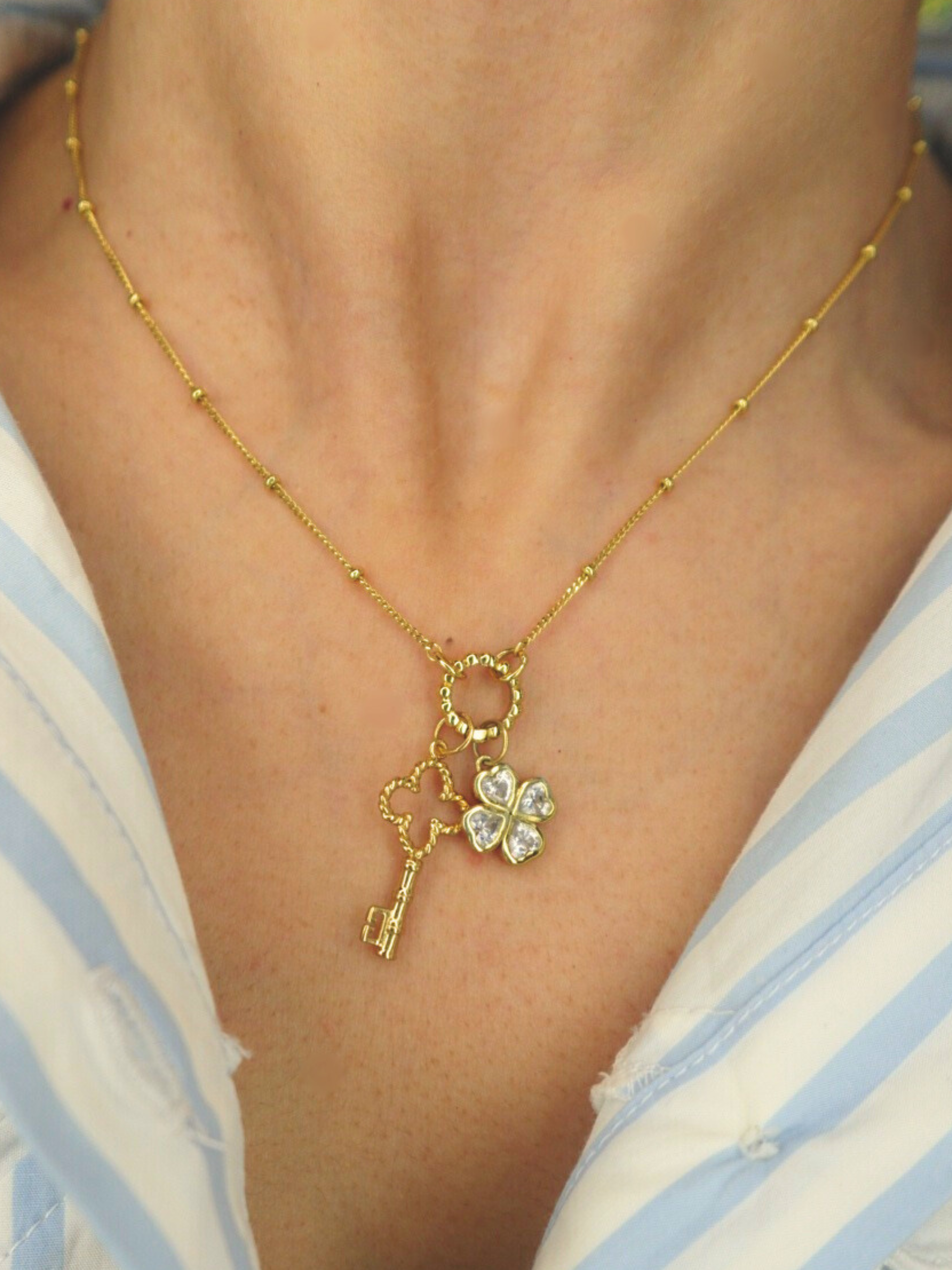 Golden necklace with a key and clover pendant on a person wearing a striped shirt