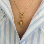 golden basket charm on a golden necklace worn by a person in a blue and white striped shirt